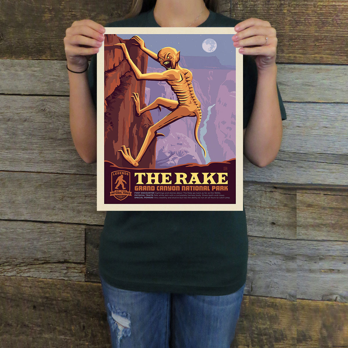 Person holding a poster of 'The Rake' at Grand Canyon National Park against a wooden background