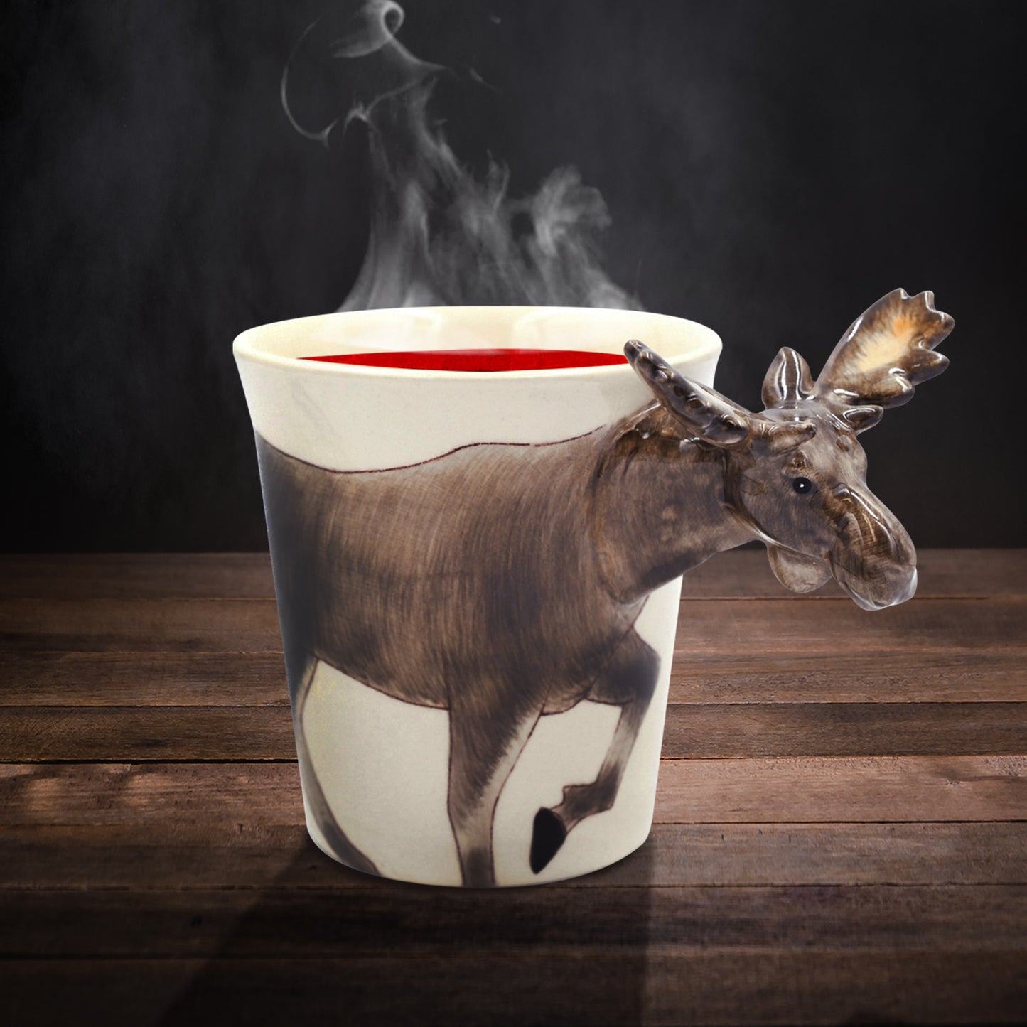 A ceramic mug on a wooden table. The mug depicts a moose drawn on the front, with the moose's head sticking out as the mug handle. The mug is filled with a red liquid, and steam is rising from the top.