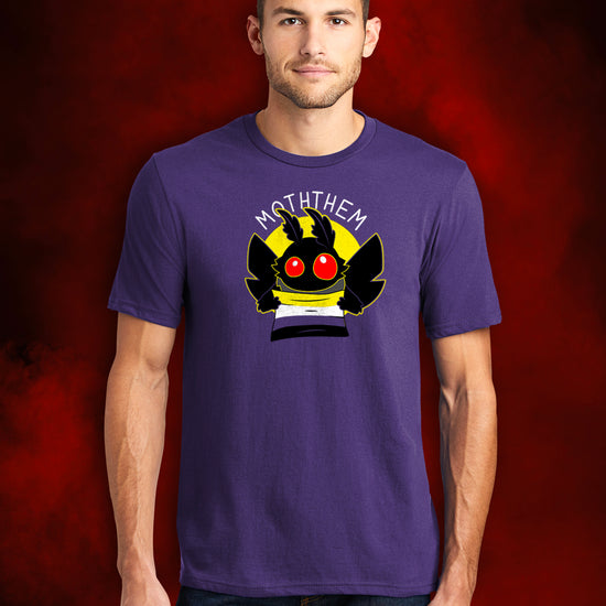 A male model wearing a purple T-shirt. A yellow circle in the center has a black moth head with red eyes, and black wings at the sides. The moth is holding a Non-binary Pride flag, in yellow, purple, white, and black. Above the image is white text saying "MOTHTHEM."  Behind the model is a smoky red background.