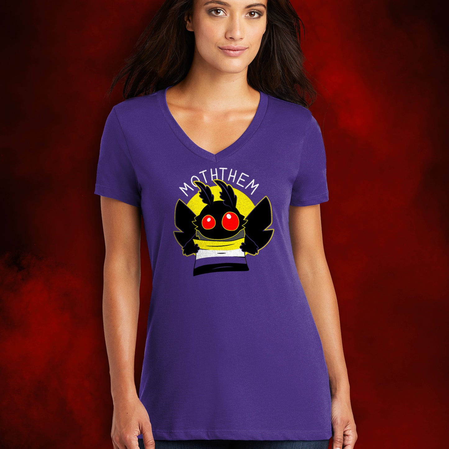 A female model wearing a purple T-shirt. A yellow circle in the center has a black moth head with red eyes, and black wings at the sides. The moth is holding a Non-binary Pride flag, in yellow, purple, white, and black. Above the image is white text saying "MOTHTHEM."  Behind the model is a smoky red background.