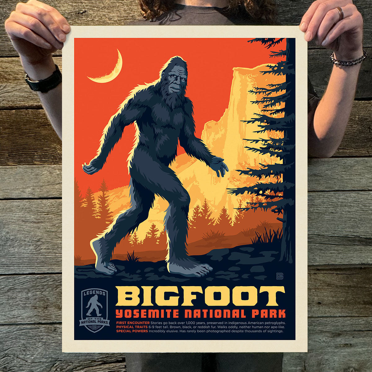 Person holding a Bigfoot Yosemite National Park poster against a wooden background