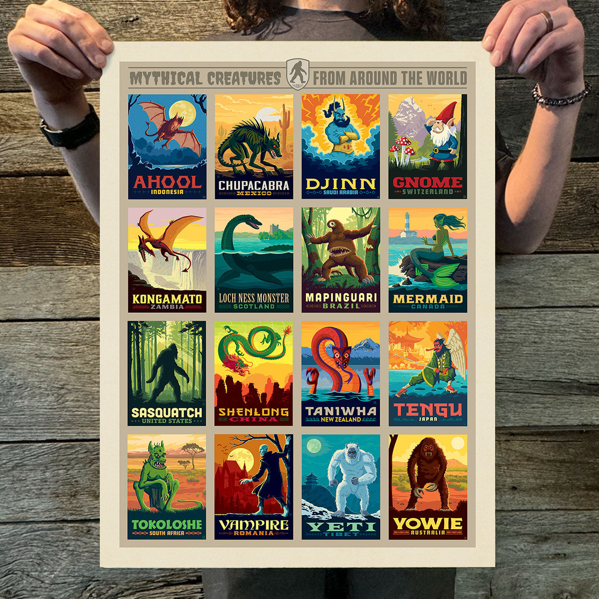 Poster of mythical creatures from around the world held by a person on a wooden background