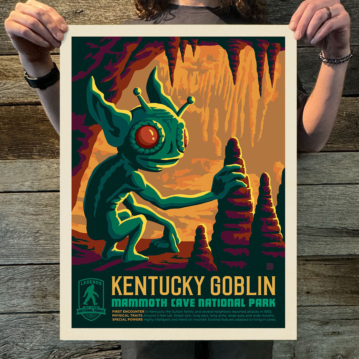 Poster of a green creature labeled 'Kentucky Goblin' held by two hands on a wooden surface.