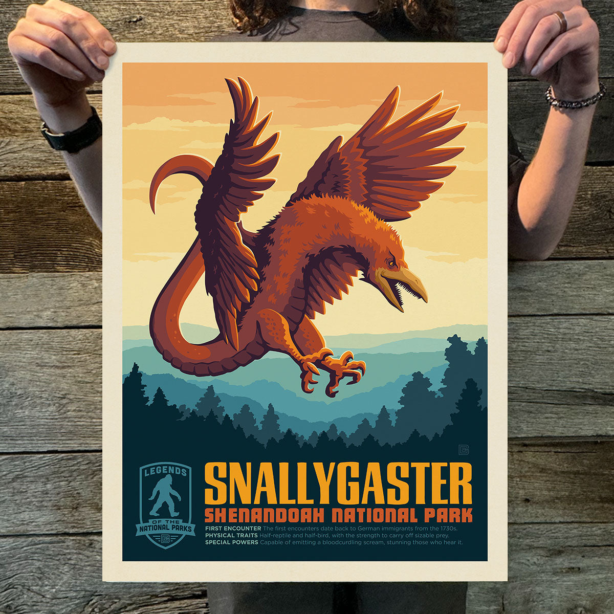 Person holding a poster of a Snallygaster creature with Shenandoah National Park text on a wooden surface.