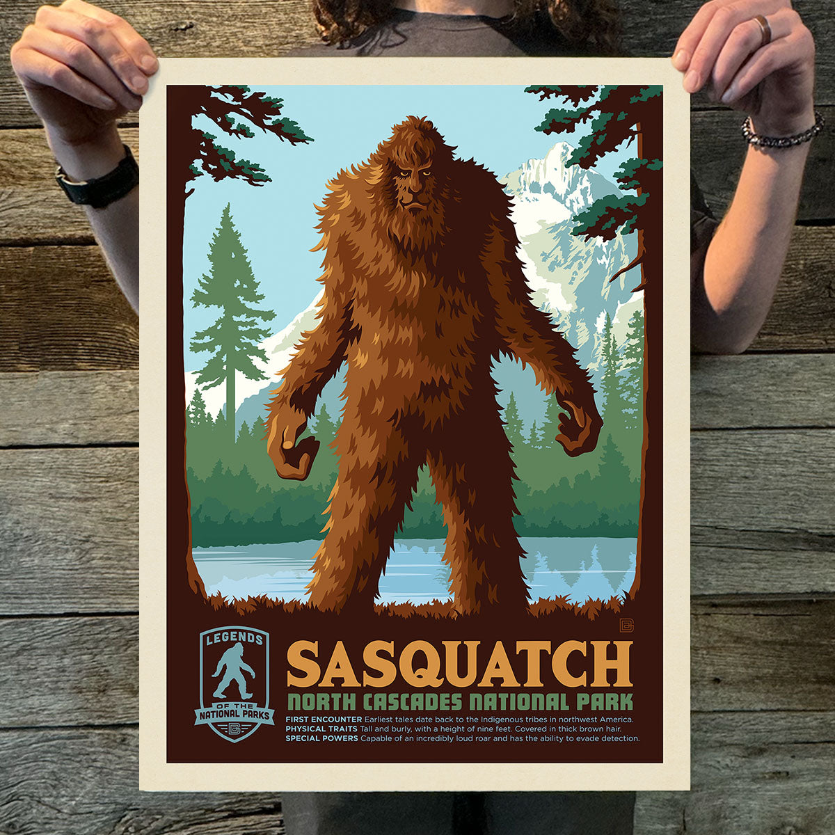 Poster of Sasquatch in North Cascades National Park held by a person on a wooden surface