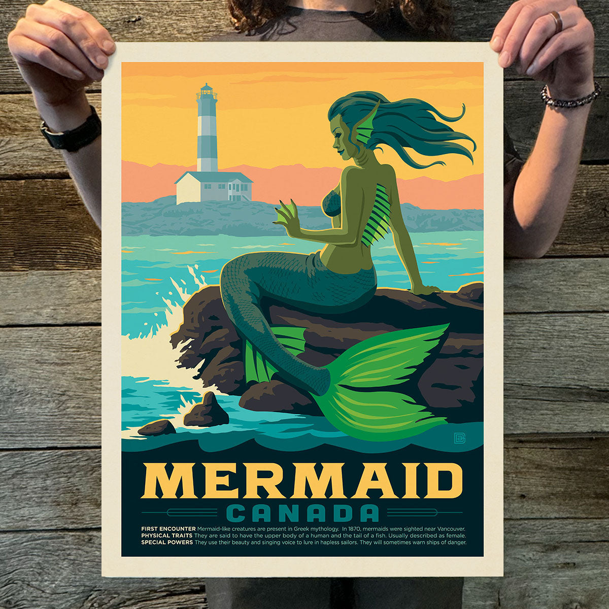 Person holding a poster of a mermaid sitting on rocks with a lighthouse in the background.