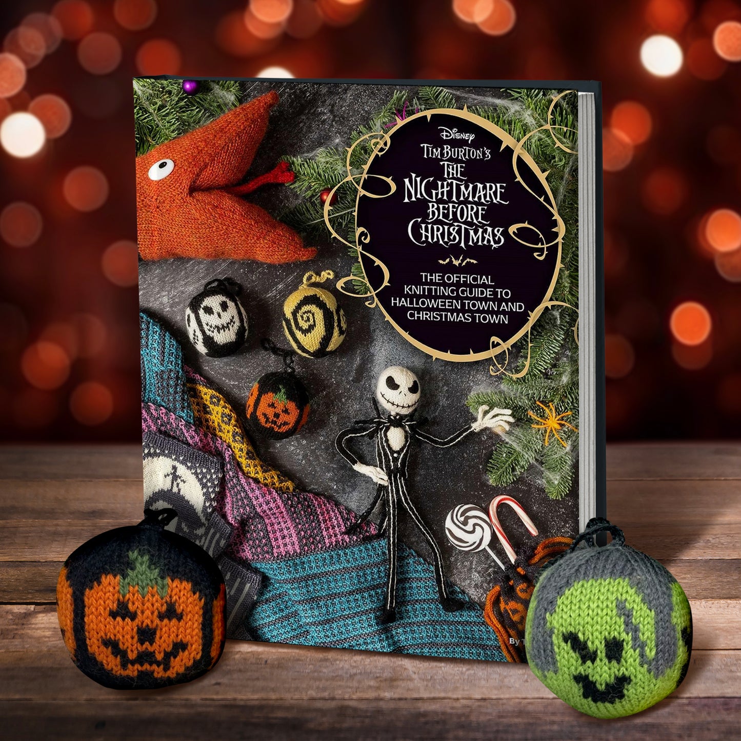 A book on a wood table. On the top right corner of the cover is a black oval, with white text saying "Tim Burton's The Nightmare before chrsitmas: the official knitting guide to halloween town and christmas town." On the cover are various knitting projects depicting characters from the film The nightmare before christmas. next to the book are knit halloween ornaments. In the background are red and orange lights.