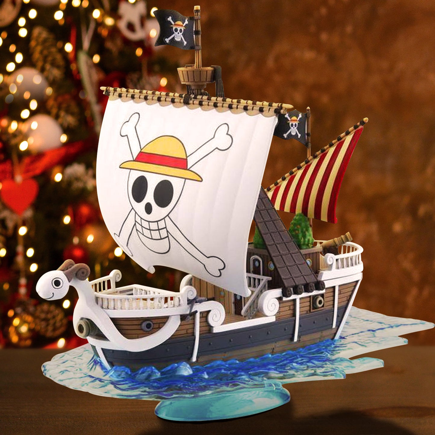 A pirate ship model from the series One Piece with skull and crossbones design, sitting on a wooden table. In the background is a decorated Christmas tree.
