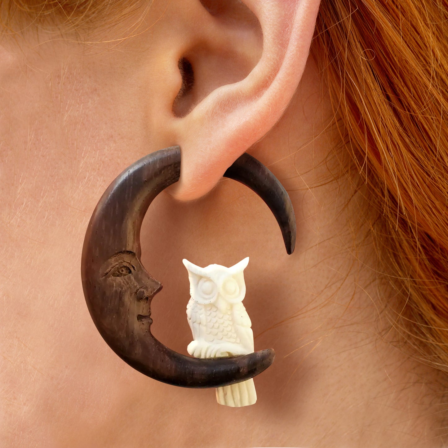 Load image into Gallery viewer, Close up of a model’s ear, with a wooden earring dangling from her earlobe. The earring is shaped like a crescent moon, with a small white owl at the bottom. The inside of the crescent moon shows a smiling face.
