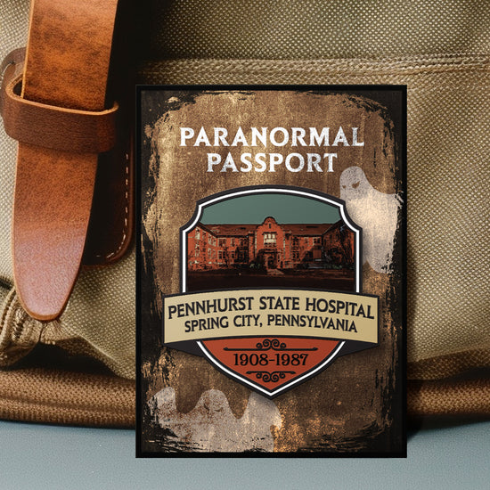 Close up on an enamel pin. The pin has a drawing of an old hospital in the center, surrounded by a stone-colored background. Two white ghost drawings are in the background. At the top is white text saying "Paranormal passport." Under the hospital drawing is text saying "pennhurst state hospital, spring city, pennsylvania. 1908-1987."