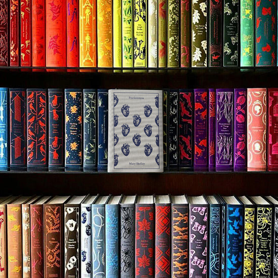 A clothbound hardcover copy of Mary Shelley's FRANKENSTEIN. It's a light grey cloth covered with a pattern of navy blue hearts. The book is sitting on a full bookshelf of other clothbounds with their colorful spines facing out.