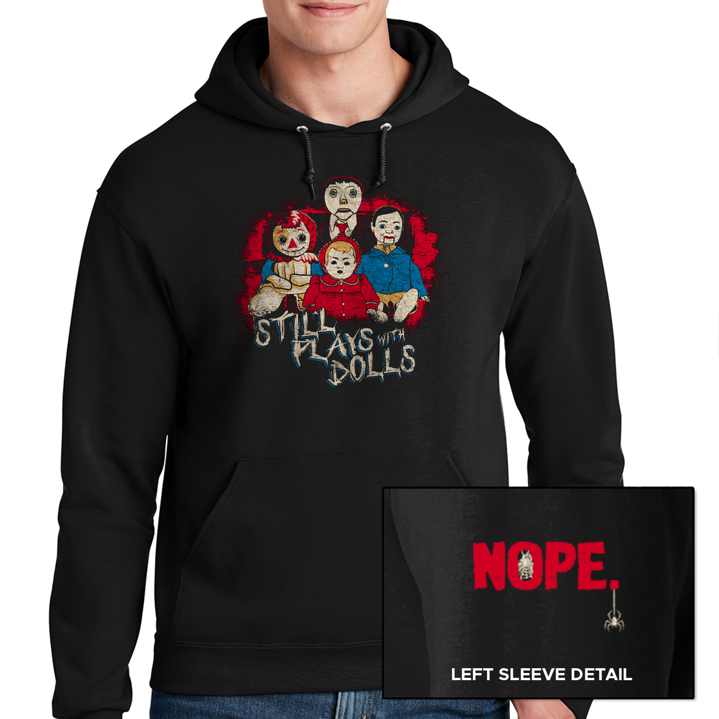 A male model wearing a black hoodie against a white background. On the shirt is a collection of creepy dolls, surrounded by red spatters. Under the dolls is white text that says "still plays with dolls." At the bottom corner is a close up of the sleeve, with red text saying "NOPE" and a small spider hanging from the last letter.