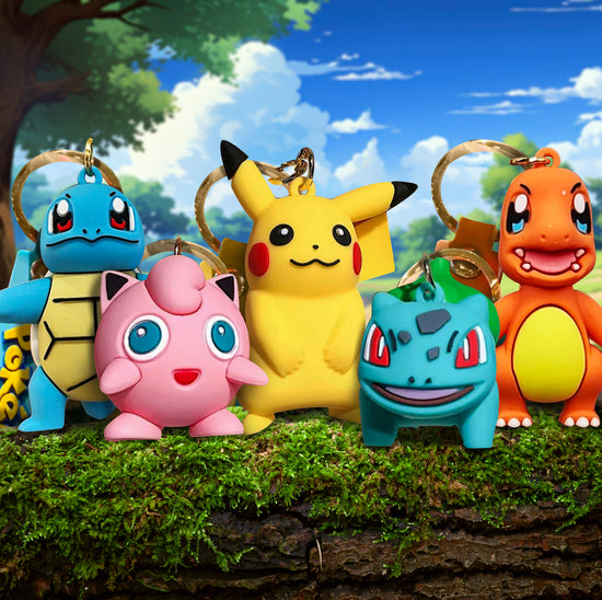 Five keychains on a moss-covered log, each depicting a different Pokemon character. In the background is a colorful drawing of a meadow, with trees and flowers in the distance.