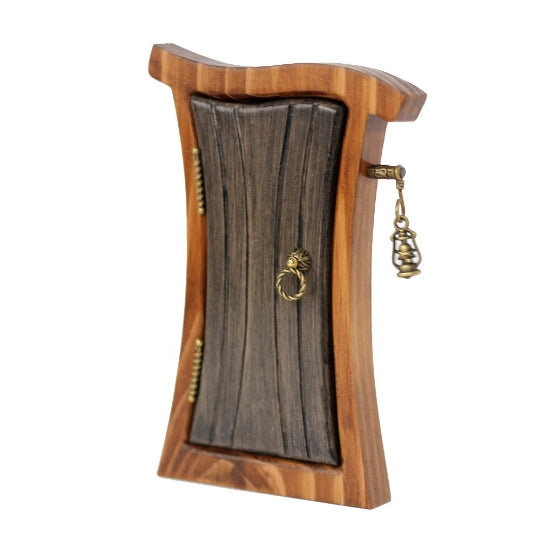A miniature, curvy wooden door and frame, against a white background. The door is a dark gray color, with brass hinges and a round doorknob on the sides. Sticking out from the frame is a tiny brass post, with a miniature lantern hanging from it.