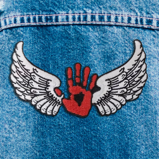 Close up of a red and white iron on patch. The patch depicts a red hand, with white angel wings at each side.