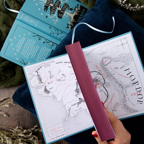 Two blue hardcover books on a wooden tray. The front cover of one book depicts a minimalist drawing of a white tree on a black ground. White text says "The Return of the King." The other book is open to show a map of Mordor.