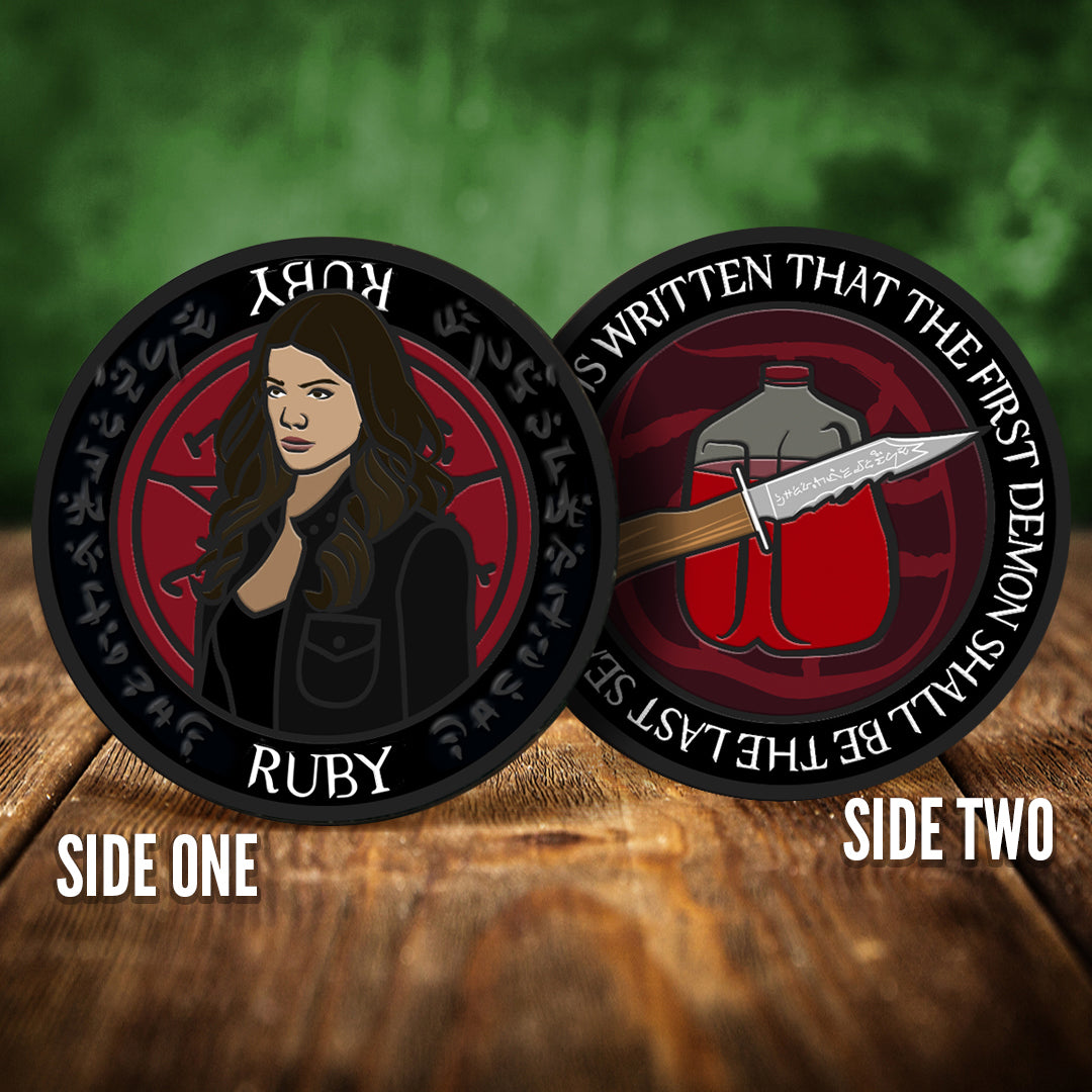 Front and back images of a challenge coin, side by side, on a wood table. The front depicts a drawing of Ruby. Behind her is a red devil's trap symbol. The back of the coin depicts a dagger in front of a gallon of blood, against a red background. White text around the edge says "And it is written that the first demon shall be the last seal."