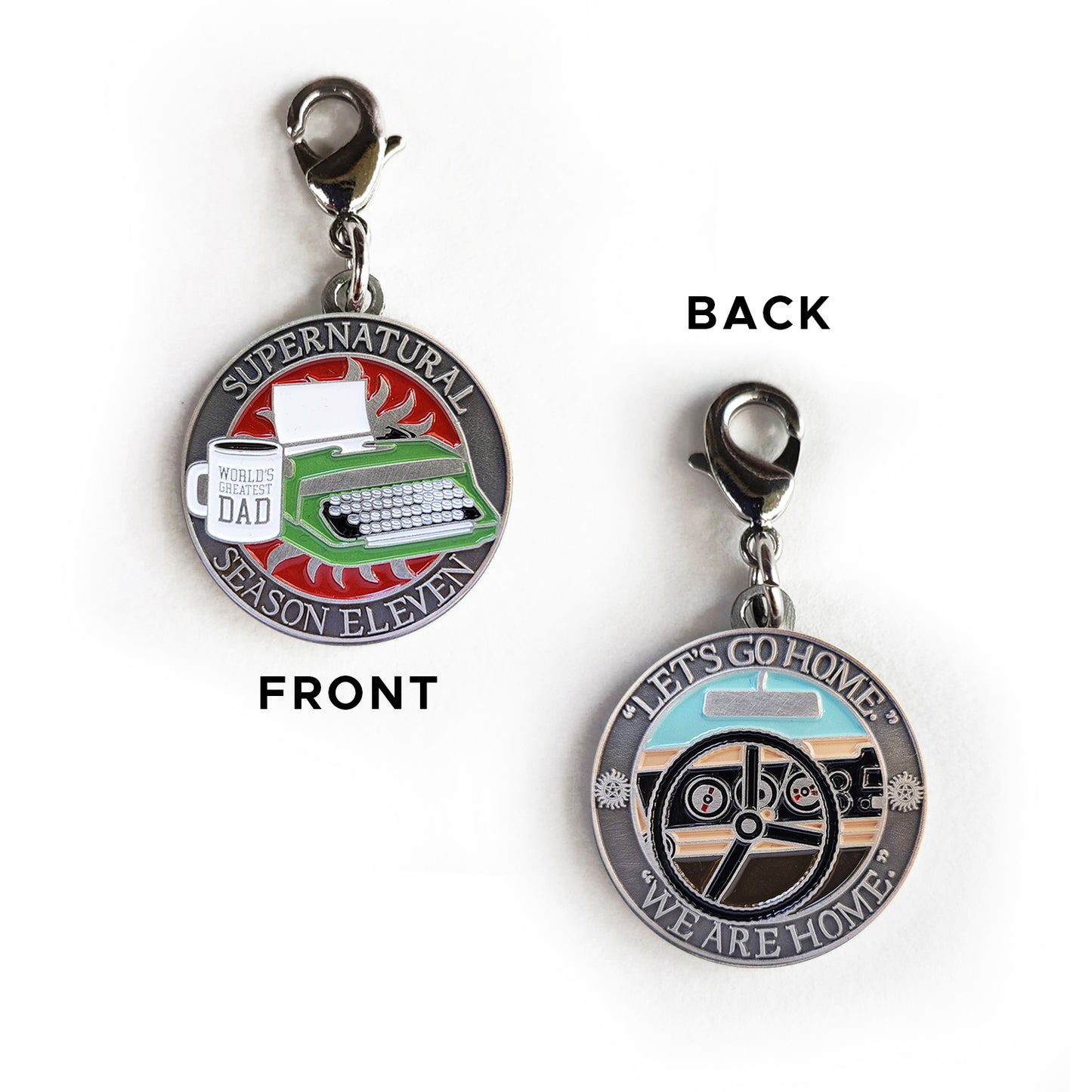 Front and back views of a brass charm. On the front is a green typewriter on a red background. Next to it is a white mug with "World's Greatest Dad" printed on it. Around the edge of the coin, raised text says "Supernatural Season Eleven." The back of the coin depicts a black steering wheel in front of a car dashboard. Around the edge is raised text saying "Let's go home... we are home."