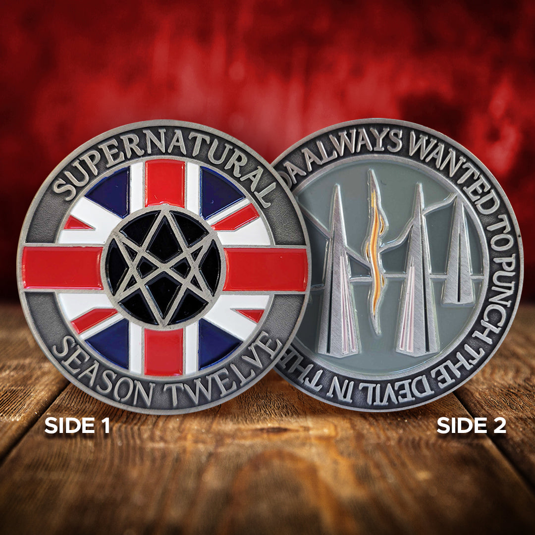 Two brass coins on a wood table. On the front are raised letters around the edge saying “Supernatural season Twelve.” In the middle is a red, white, and blue Union Jack flag, with a Men Of Letters symbol at the center. On the back of the coin are raised letters around the edge saying “I kinda always wanted to punch the devil in the face.” In the middle is are tall triangles rising from a grey background, with a read and yellow line down the center. Behind it is a red wall