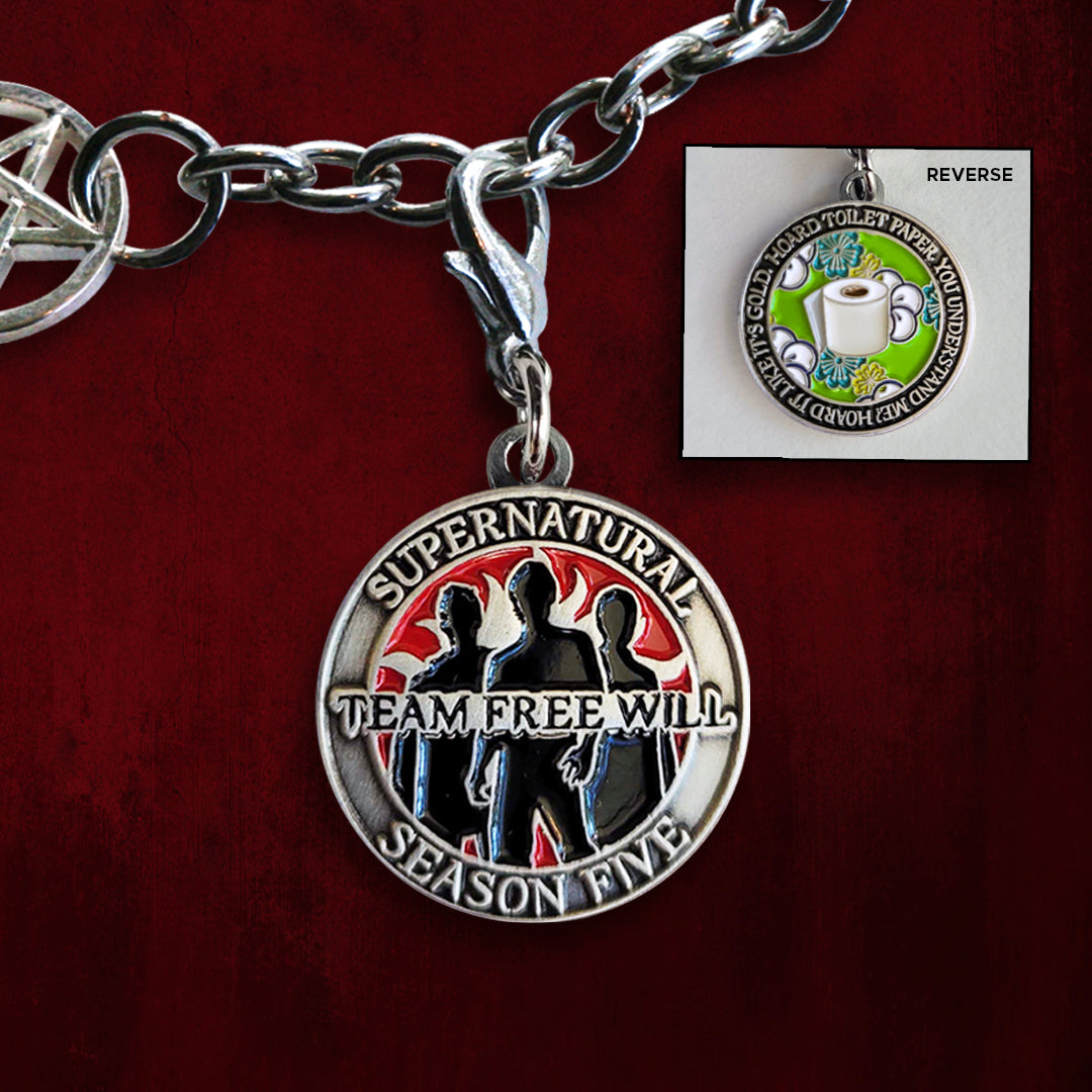 A brass coin charm with "Supernatural season five", "Team Free Will", and three male sillhouettes against a red background on one side and "Hoard toilet paper. You understand me? Hoard it like it's gold." with a green flowered background and a roll of toilet paper on the other.