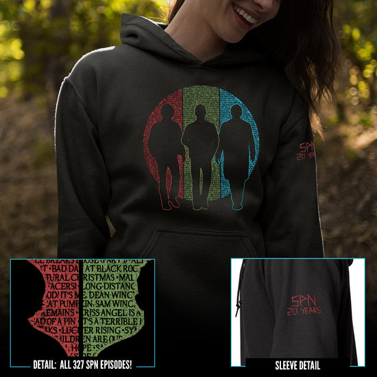 A female model wearing a black unisex hoodie. The shirt features silhouettes of Sam and Dean Winchester and Castiel. Behind them is a circle split into vertical thirds - a red slice behind Sam, green behind Dean, and blue behind Castiel. The circle is filled with the titles of all 327 episodes of Supernatural in black font. One sleeve reads 'SPN 20 YEARS' in a capital font with a 'carved' effect.