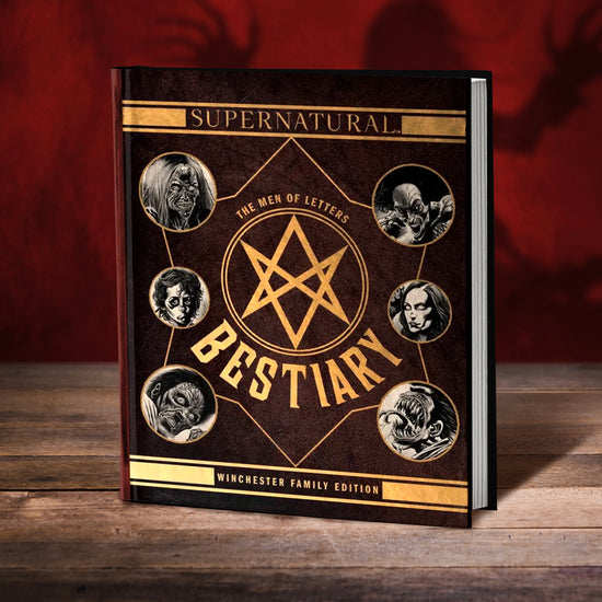 A brown book on a wood table. On the top of the cover is yellow text saying "Supernatural," surround by yellow block lines. In the center is a yellow Men of Letters symbol, with yellow text around it saying "the men of letters bestiary." Around symbol are black and white drawings of monsters from the TV series Supernatual. At the bottom is yellow text saying "winchester family edition," surrounded by yellow block lines. In the background is a dark red wall with a creepy shadow.
