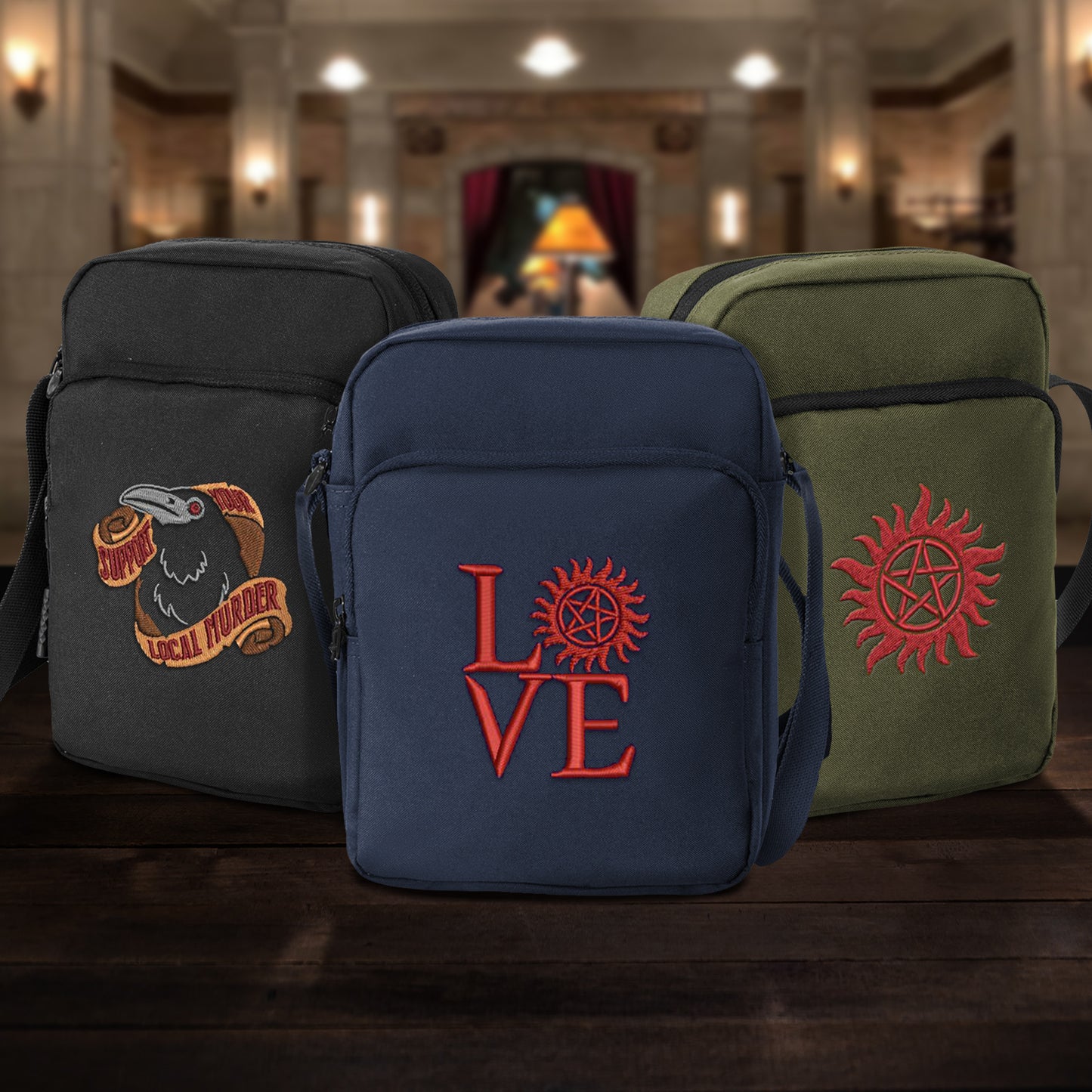 Three cross body bags side by side on a wooden table. One bag is black, one is dark blue, one is olive green. On the front  of the black bagis a black crow with red eyes, with gold paper scrolls above and below. Red text says "support your local murder." The front of the blue bag has red text saying "love," with the "O" replaced by the anti-possession symbol. The green bag has the anti-possession symbol in red.