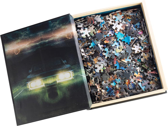 An image of a book on a white background, opened to reveal a hollow space filled with jigsaw puzzle pieces. On the inside cover is an image of a 1967 Impala on a dark road, underneath lightning bolts in the sky.