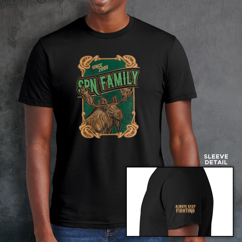 A male model wearing a black t-shirt, against a grey wall. On the front of the shirt is a green and brown rectangle with a brown frame. A brown moose is depicted at the bottom. Green text says "SPN Family" across the middle. At the top is light brown text saying "Since 2005." At the bottom right corner is a close up of the left sleeve, with yellow text saying "Always Keep Fighting."