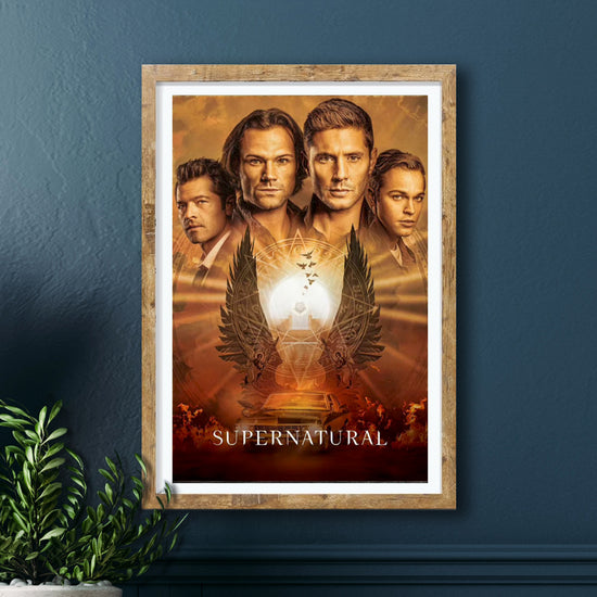 A framed print against a dark blue wall. The print depicts Sam, Dean, Castiel, and Jack from the TV series Supernatural, all drawn in sepia colors. Below the characters is a set of angel wings under a bright circle, overlayed by a faint devil's trap. White text at the bottom says "supernatural." Beneath the text is a drawing of a black chevy impala.