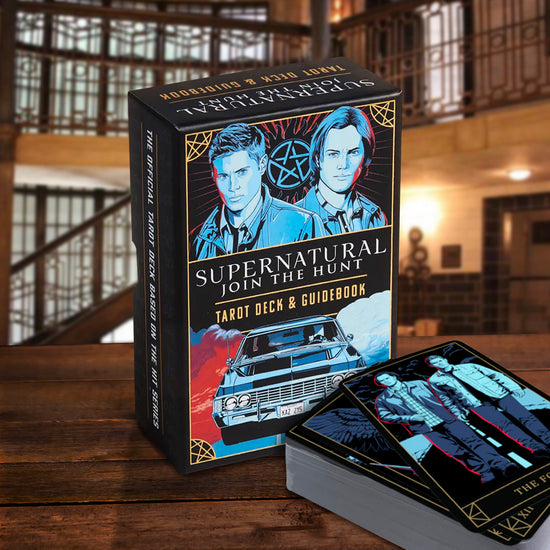 A box of Tarot cards sitting on a table "in" the Men of Letters Bunker. The box reads "Supernatural - Join the Hunt - Tarot Deck & Guidebook" and features Sam and Dean Winchester, the Impala, and an anti-possession symbol.