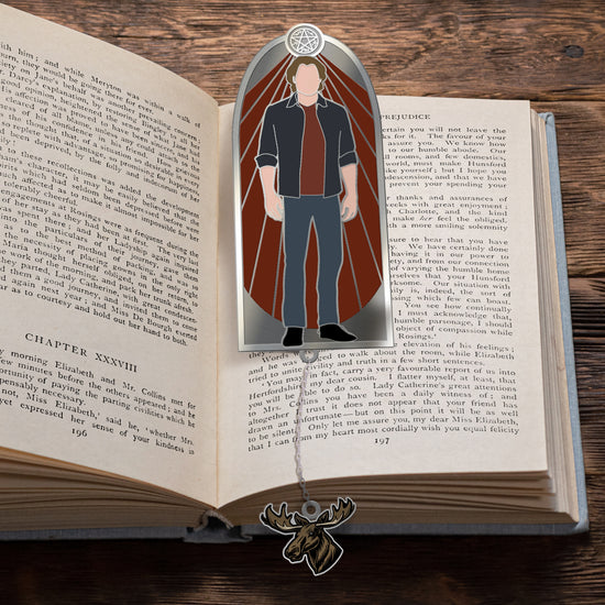 a bookmark on an open book. The bookmark depicts Sam Winchester against a red background. At the bottom of the bookmark is a moose-shaped charm attached to a chain.