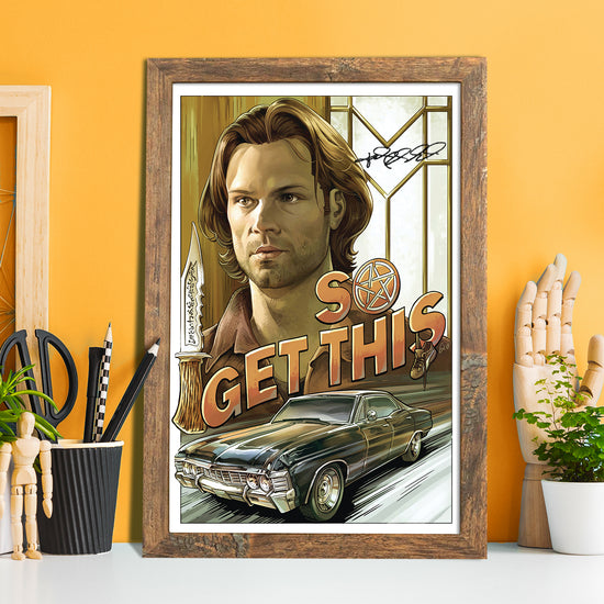 A framed drawing of Sam Winchester's face. Under the face is a 1967 Chevy Impala, with orand text above it saying "so get this." The O in the text contains the anti-possession symbol. At the top of the drawing is Jared Padalecki's autograph. Behind the drawing is a yellow wall. On either side are artist's tool and wooden models.