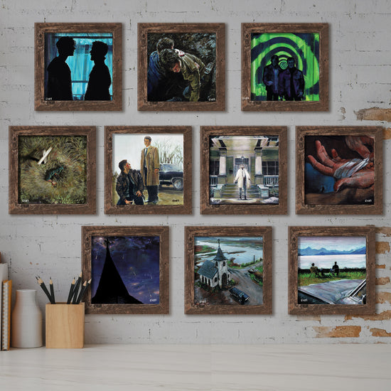 A series of framed lithographs mounted on a light grey brick wall. Each lithograph depicts an image taken from the first ten seasons of the TV series "Supernatural." Underneath the lithographs are a white vase, and a wooden holder filled with drawing pencils.
