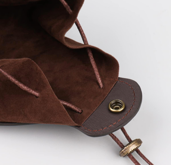 Close of view of a brown leather pouch on a white background, zoomed in to a brass button and drawstring used to close the bag.