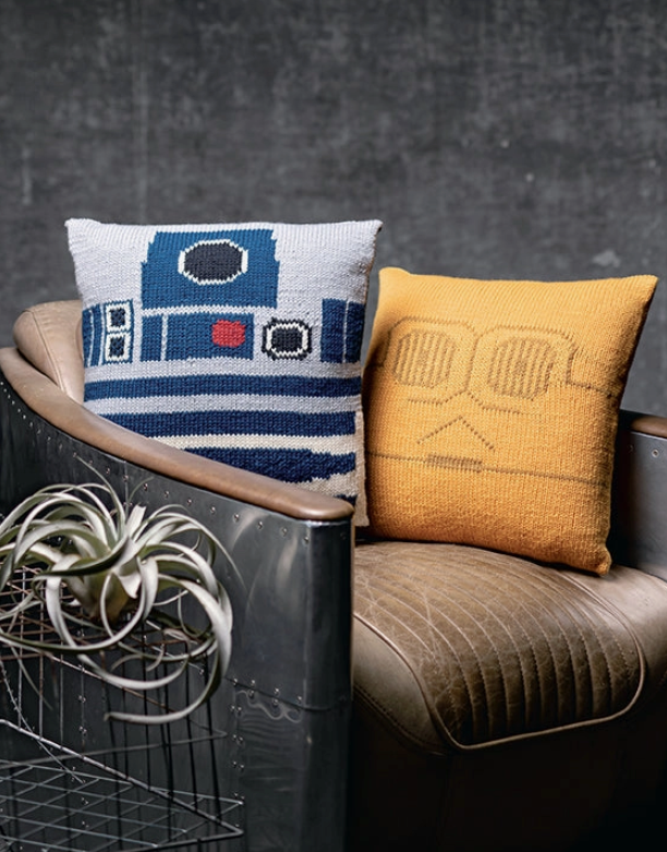 Two knit throw pillows on a leather chair. One pillow is the blue and white face of R2D2, the other is the gold face of C3PO, two droids from the Star Wars movies.