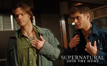 A postcard with an image of Sam and Dean Winchester from the TV series “Supernatural.” They are both showing tattoos printed in their chests.