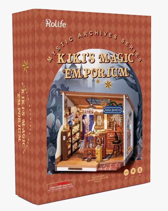 A brown box with an image of the assembled dollhouse on the front. The title “Kiki’s Magic Emporium” is printed on the top in pale yellow text.