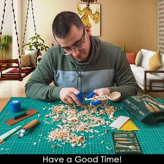 Load image into Gallery viewer, A man in a green and grey sweater sites at a table with the carving kit in front of him. He is carving the handle of the spoon. Under the image is text saying &amp;quot;Have a good time!&amp;quot;
