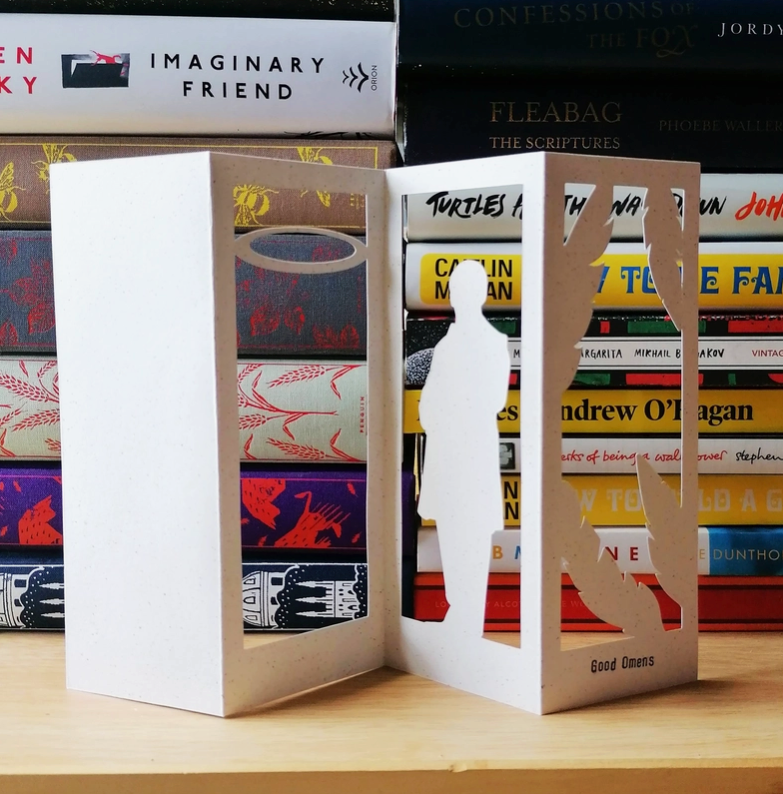 Load image into Gallery viewer, An image of a white bookmark standing in front of a pile of books. The bookmark is cut to depict Aziraphale, an Angel from the series &amp;quot;Good Omens.&amp;quot;
