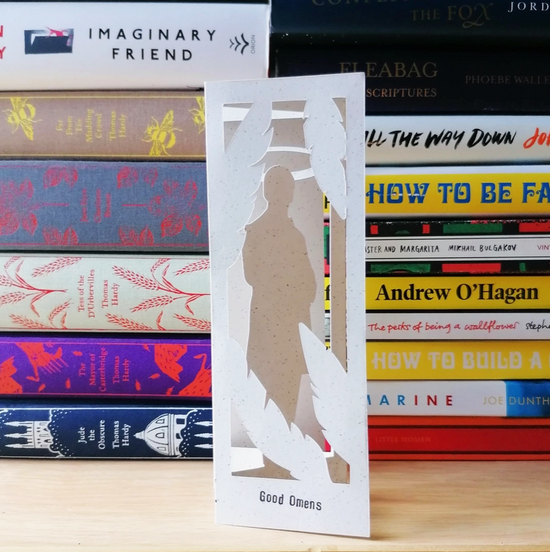 Load image into Gallery viewer, An image of a white bookmark standing in front of a pile of books. The bookmark is cut to depict Aziraphale, an Angel from the series &amp;quot;Good Omens.&amp;quot;
