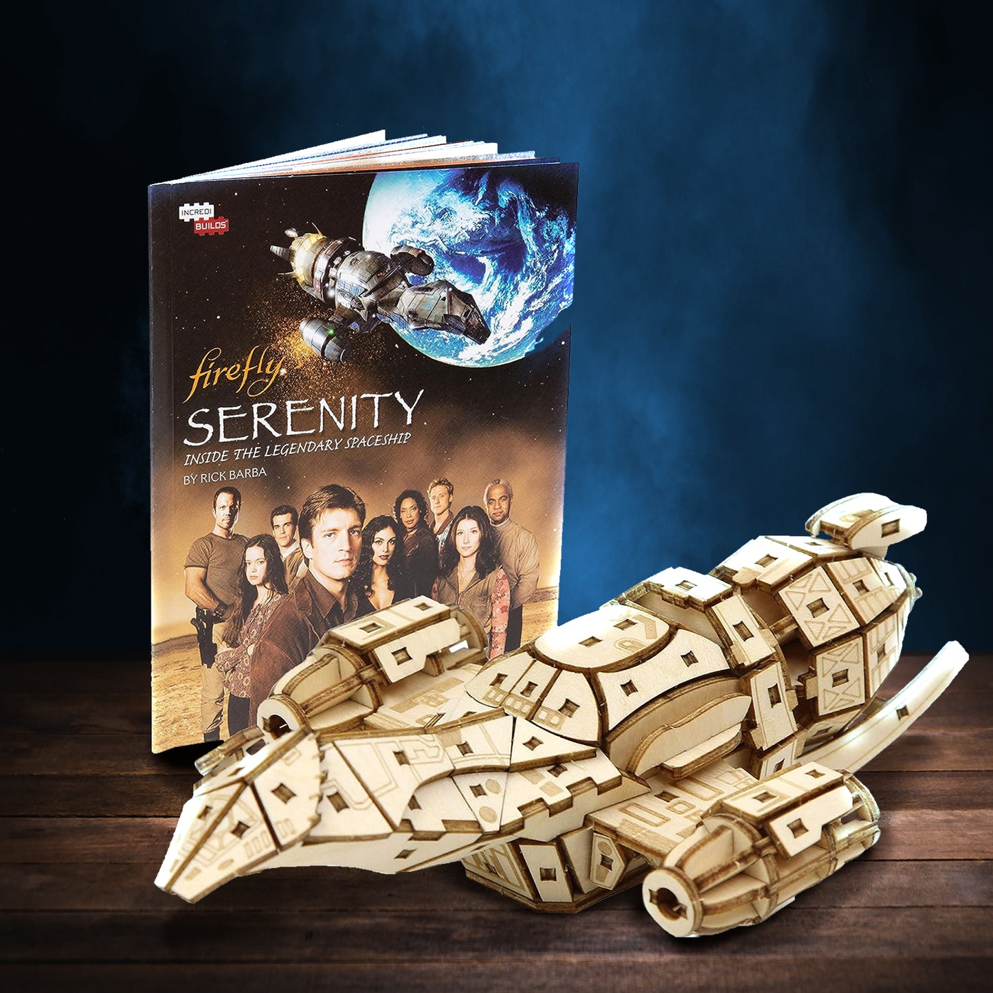 A wooden model of the spaceship Serenity, from the TV series "Firefly," on a wooden table against a smoky blue background. Next to the model is a booklet with building instructions, with the "Firefly" cast on the cover.