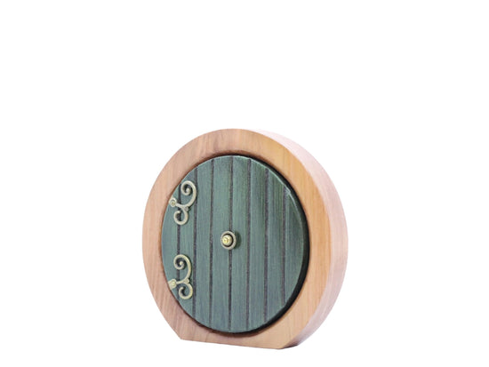 A round wooden doorframe with a green door, against a white background. The door has ornate brass hinges at the side, and a brass doorknob in the center. 