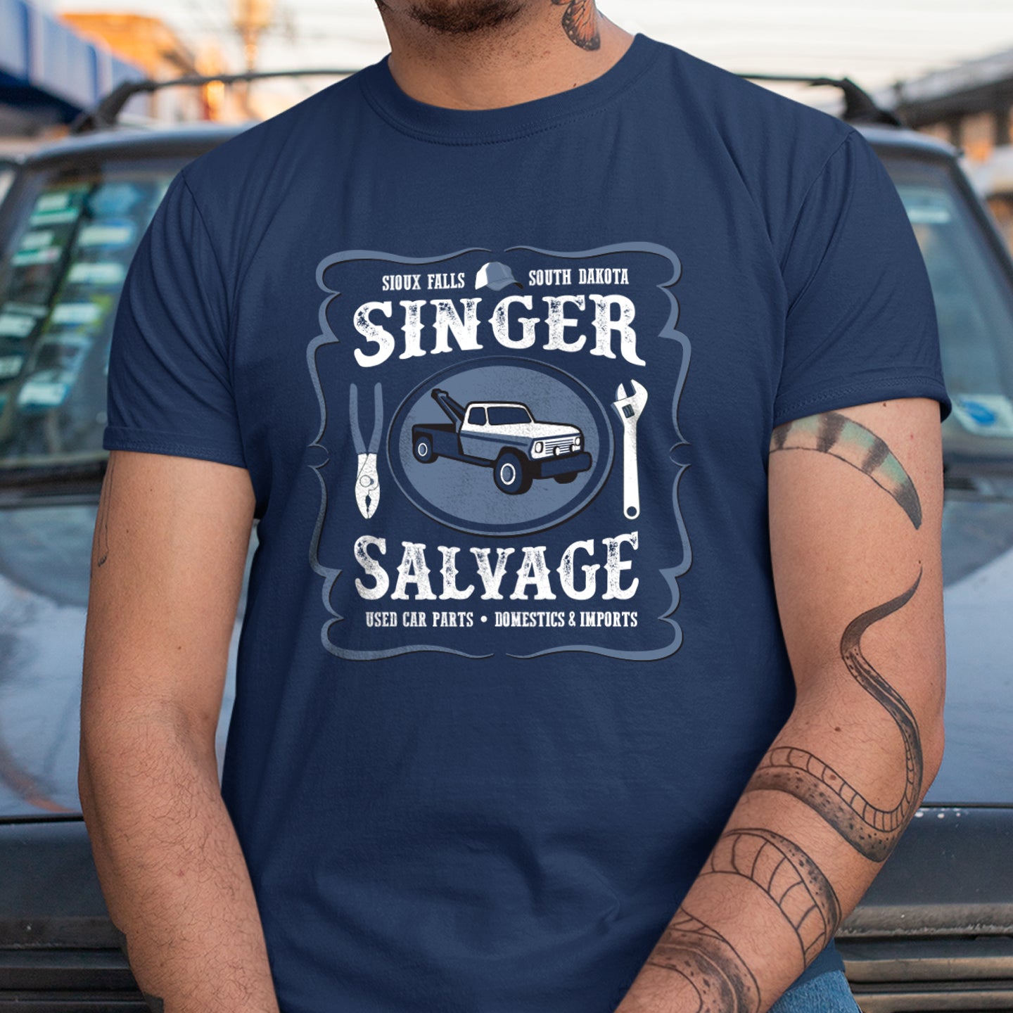 A model in a blue tee shirt with a Singer Salvage logo on the front. The logo includes a tow truck and mechanic tools.