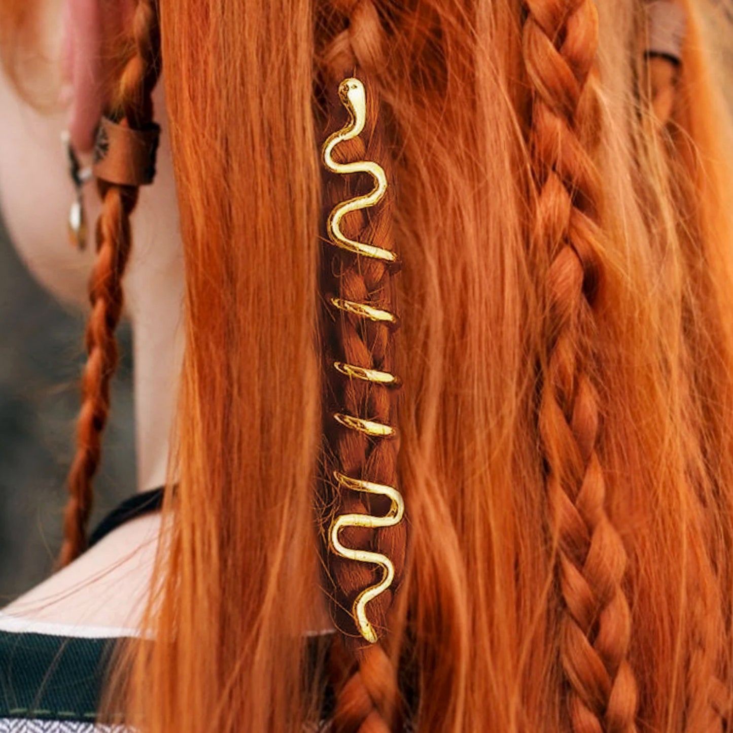 An image of a model with long red hair, partially in braids. Small bronze hair cuffs, shaped like snakes, are interwoven into her braids.