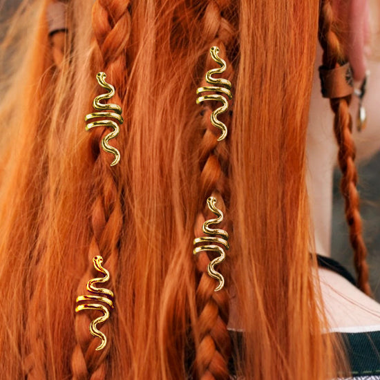 An image of a model with long red hair, partially in braids. Small gold hair cuffs, shaped like snakes, are interwoven into her braids.