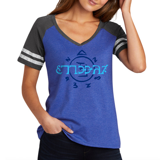 A Female model wearing a blue V-neck shirt with grey sleeves. The front of the shirt has light blue runes, which spell out the word "funnier" in the angelic language Enochian. On the left sleeve is a pair of black wings with white and blue text that says "SPN 20 years."