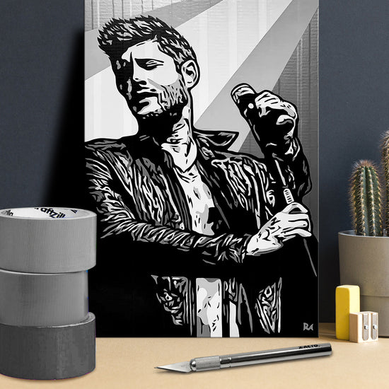 A poster made of layered pieces of duct tape, depicting actor Jensen Ackles holding a microphone. In front of the poster is an X-acto knife and rolls of duct tape.