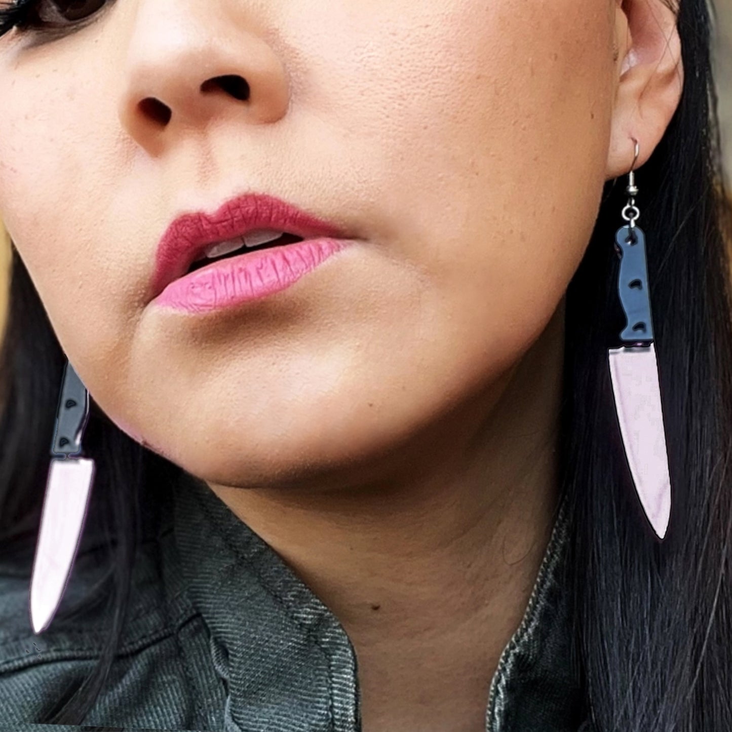 Close up a woman's face. In her ears are earrings shaped like chef's knives.