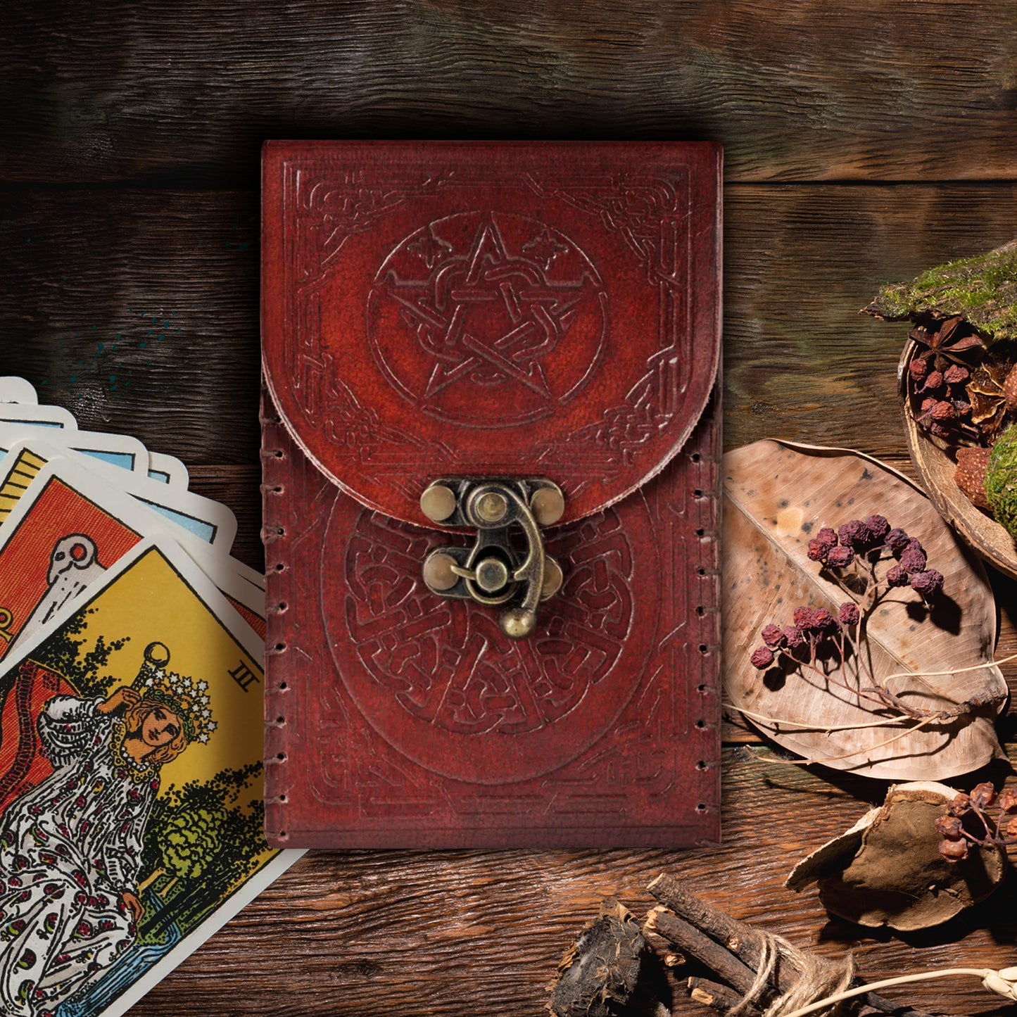 A reddish-brown leather tarot card holder with a brass closure clasp. The leather is embossed with a tarot-art-style pentagram on the front flap, and a Celtic knot on the bottom front.
